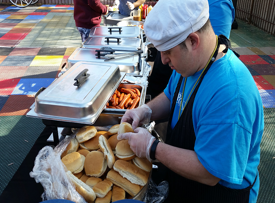A man preparing hamburger and hotdog buns at an outdoor bbq.